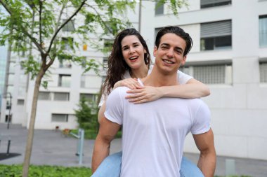 Güzel genç çift sarılma ön görünümü, kamera bakıyor ve açık havada ayakta iken gülümsüyor