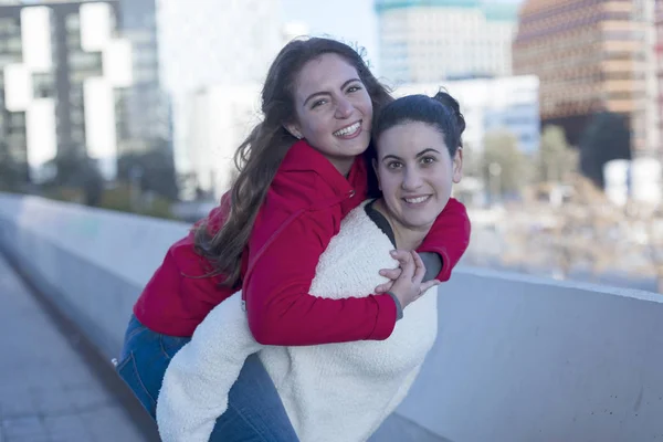 Vista frontale dei migliori amici sorridenti ragazze a cavalluccio all'aperto in città — Foto Stock