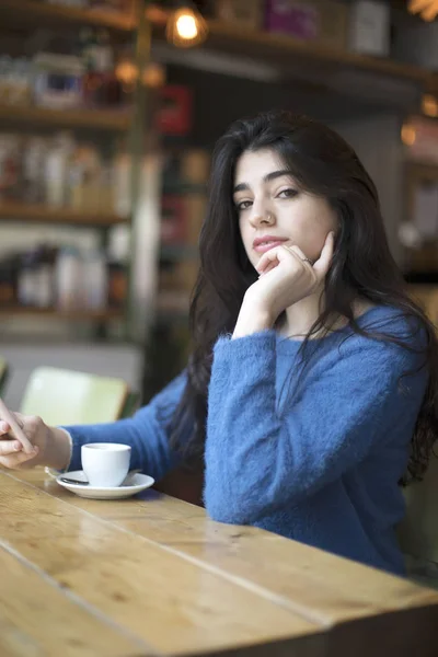 Mujer joven bebiendo café y utilizar su teléfono inteligente sentado en el interior de la cafetería urbana. Café ciudad estilo de vida. Retrato casual de hermosa chica — Foto de Stock