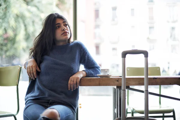 Mujer joven y moderna en jersey azul sentada en un café mientras mira hacia otro lado , — Foto de Stock