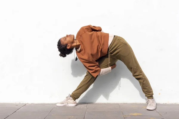 Elegante giovane attraente corridore donna in abbigliamento sportivo nero facendo routine di riscaldamento all'aperto prima di correre contro il muro — Foto Stock