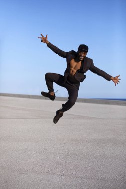 Ön görünümü kentsel arka planda atlama rahat giysiler giyen genç siyah adam.