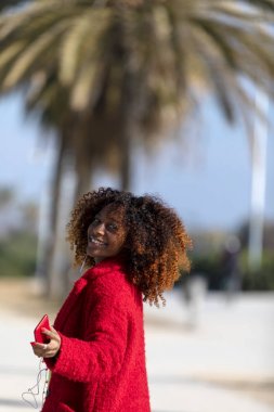 Genç gülümseyen kıvırcık Afro kadının ön görünümü açık havada gülümseyen ve güneşli bir günde uzakta görünümlü iken