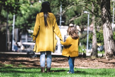 Anne ve küçük kızı, sarı ceket giymiş, yürüyüş ve parkta el ele tutuşarak Arka görünümü