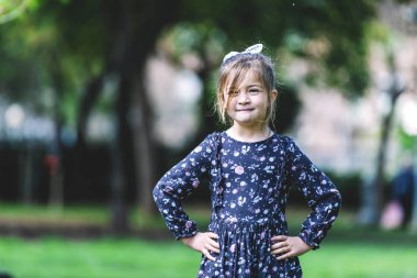 Front view of happy little girl in dress standing in the park