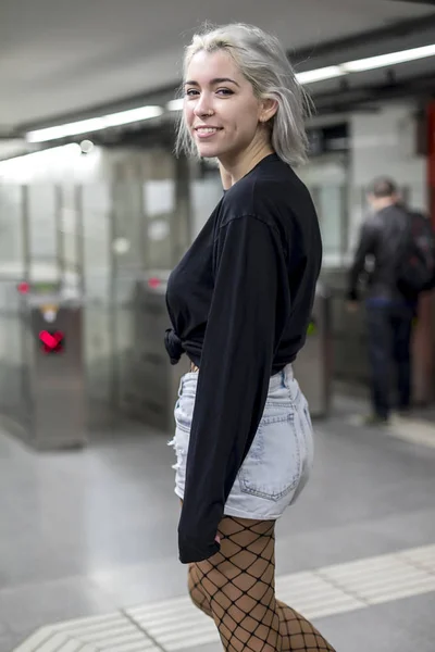 Back view of a young woman in shorts holding a long board while standing on mechanic stairs at night — Stock Photo, Image