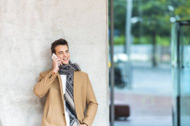 Genç adam arıyor. Gri arka planda dururken cep telefonu kullanan orta yaşlı bir adam. Gri duvara yaslanan bir adam başka tarafa bakıyor ve gülümsüyor