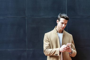 Genç adam telefon mesajı yazıyor. Gri arka planda dururken cep telefonunda yazan orta yaşlı bir adam.