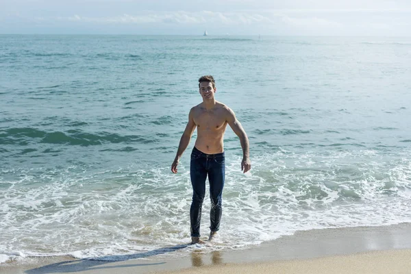 Giovane uomo muscoloso bello in riva al mare in una giornata di sole — Foto Stock