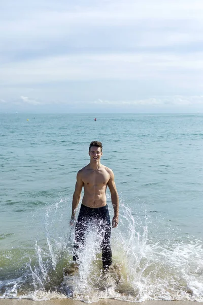 Giovane uomo muscoloso bello in riva al mare in una giornata di sole — Foto Stock