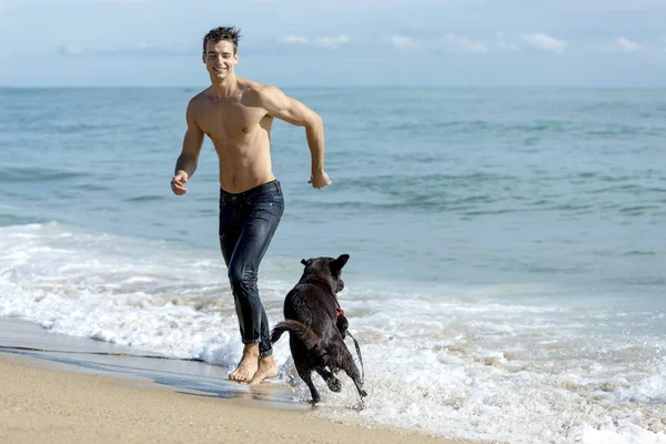 Young caucasian male playing with dog on beach during sunrise or sunset. — ストック写真