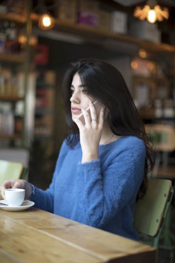 Bir kafede masada otururken akıllı telefon kullanarak ve uzağa cam bakarak güzel genç bayan portresi