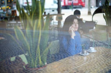 Kafede otururken akıllı telefonla konuşan kadın pencereden görüldü