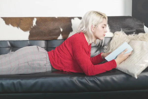 Mujer acostada en el sofá en casa leyendo un libro —  Fotos de Stock