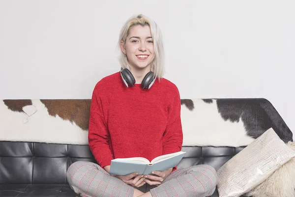 Retrato de una joven feliz con libro sentado en el sofá en casa — Foto de Stock