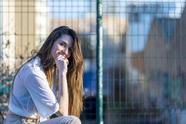 Kamera açık havada bakarken bir bankta oturan gülümseyen güzel sarışın kadın Yan görünümü