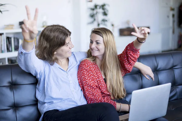 Niñas adolescentes felices sentadas en un sofá con un ordenador portátil haciendo signo de victoria — Foto de Stock