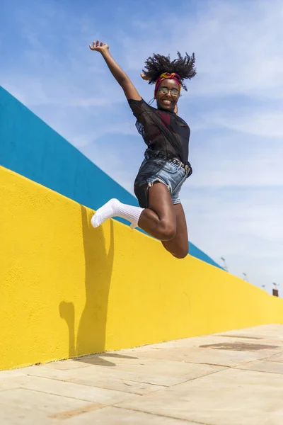 Felice giovane donna afro-americana bella saltare contro il muro, mentre sorridente e guardando la fotocamera . — Foto Stock