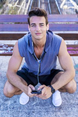 Mutlu koşucu kameraya bakarken çömelmiş müzik dinliyor.