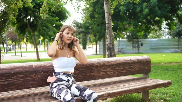 공원 벤치에 앉아 음악을 듣고 있는 젊은 여자 — 스톡 사진