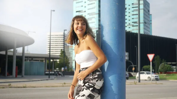 Young smiling woman sleeveless standing in the street while looking away against city buildings