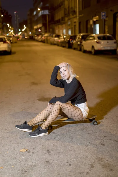 Vista frontal de mujer joven en pantalones cortos en un tablero largo mientras mira la cámara en la noche en la ciudad — Foto de Stock