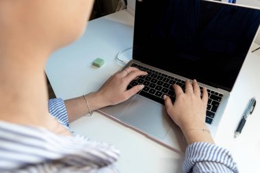 Genç bir kızın en iyi görüntüsü, beyaz ofis masasının üzerinde dizüstü bilgisayarda klavye yazması..
