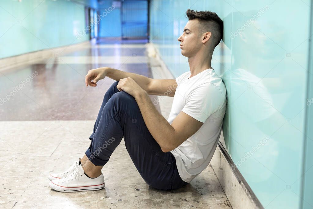 Young guy in depression sitting on ground street subway