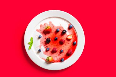 Çilek ve böğürtlen buzlu dondurmanın üstünde kırmızı arka planda.