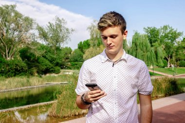 Sarışın genç erkek dışarıda cep telefonu kullanıyor.