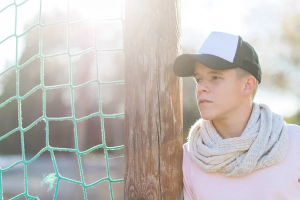 Portrait of a serious young male leaning behind a net fence while looking camera