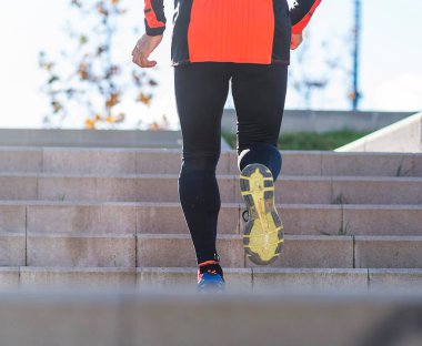 Güneşli bir günde, bir parkta merdivenlerden inip çıkan Kafkasyalı son sınıf bir sporcunun arka görüntüsü.