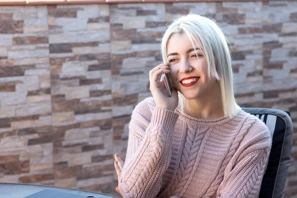 Dışarıda cep telefonuyla konuşan mutlu sarışın genç kadın.