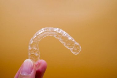 Turuncu arka plan üzerinde diş düzenleme ameliyatı için Invisalign tutucu el