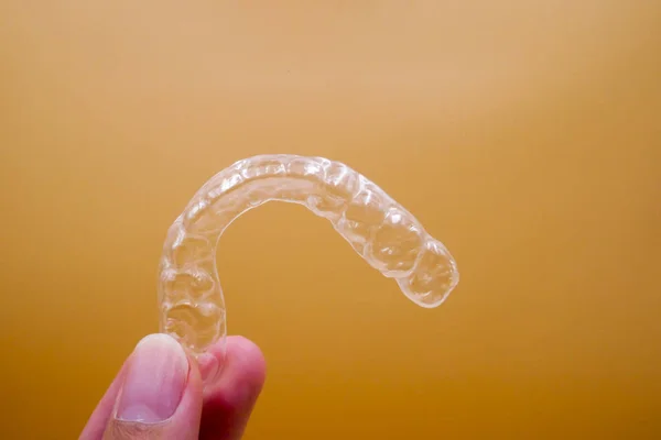 Ręka na uchwyt Invisalign do operacji ułożenie zębów na pomarańczowym tle — Zdjęcie stockowe