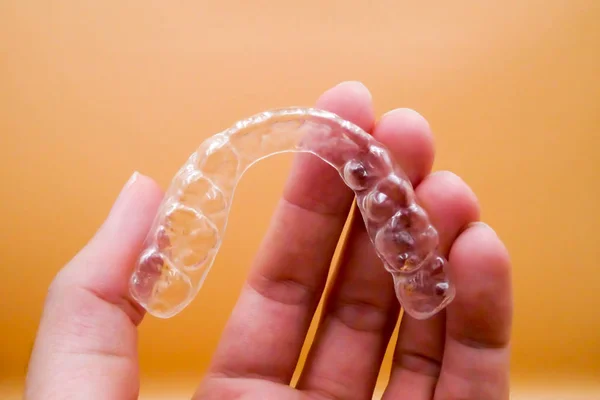 Ręka na uchwyt Invisalign do operacji ułożenie zębów na pomarańczowym tle — Zdjęcie stockowe