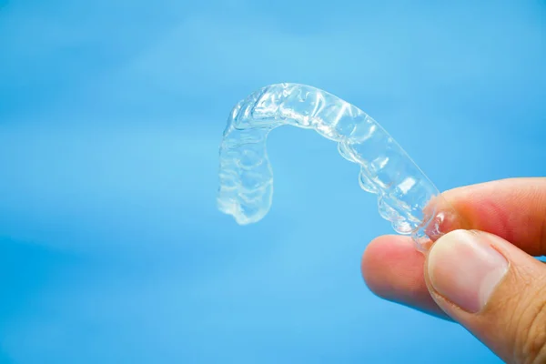 Mână care deține dinți de reținere din plastic clar, care izolat pe fundal cerul albastru . — Fotografie, imagine de stoc