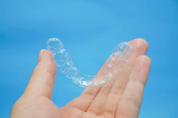 Mão segurando dentes de plástico transparente retentor que isolado no fundo azul — Fotografia de Stock