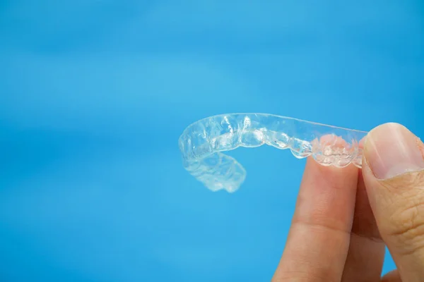 Hand holding clear plastic retainer teeth that isolated on blue background — Stock Photo, Image