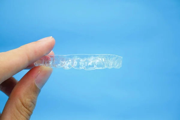 Ruka držící zřetelné plastové upínací zuby izolované na modrém pozadí — Stock fotografie