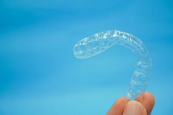 El mavi arka plan üzerinde izole net plastik tutucu dişleri tutarak — Stok fotoğraf