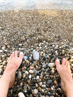 Kayalık deniz plajı arka planda pembe oje ile kadın pedikürlü bacaklar yakın ayak ve ayak parmakları