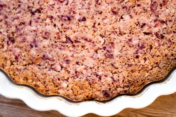 Cake or baked pudding of cottage cheese with red bilberry on white baking dish on wooden background