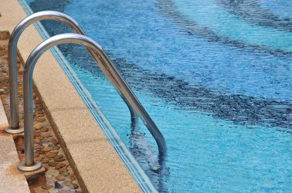 Grab bar ladder in Swimming pool, Blue spa swimming pool with clean water and beachfront background.