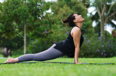 Yoga bhujangasana kobrası beyaz kostümlü bir kadın tarafından parktaki yeşil çimlerde poz verdirilmiş.