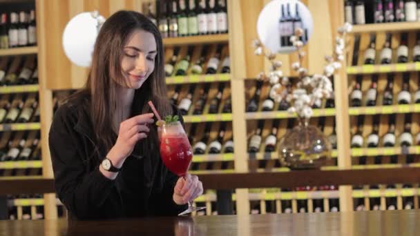 Una giovane ragazza beve un cocktail su un tavolo in un ristorante di moda, una giovane ragazza con un cocktail esotico rosso a un tavolo in un ristorante o bar, una donna che beve cocktail esotico rosso — Video Stock