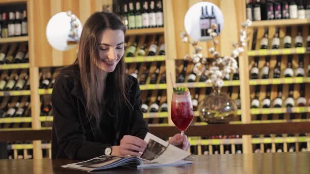 Uma jovem bebe um coquetel em uma mesa em um restaurante de moda, uma jovem com um coquetel vermelho exótico em uma mesa em um restaurante ou bar, uma mulher bebendo um coquetel vermelho exótico — Vídeo de Stock
