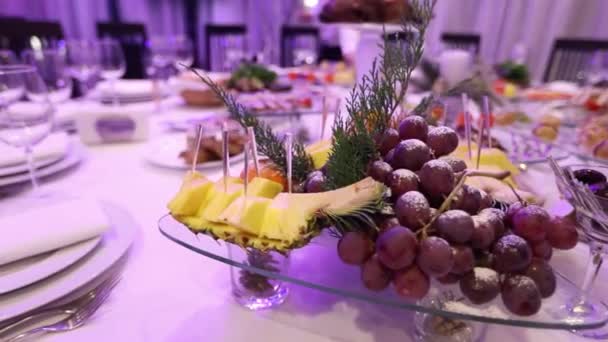 Φρούτα και τρόφιμα για το Συμπόσιο τραπέζι στο εστιατόριο, κομμάτια του ανανά και τσαμπιά από σταφύλια σε πίνακα Συμπόσιο, διακόσμηση της αίθουσας συμποσίων, εσωτερικό εστιατόριο — Αρχείο Βίντεο