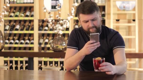 Man hipster dricka en röd dricka i en restaurang eller ett café, en ung man med en smartphone medan du dricker en röd cocktail — Stockvideo