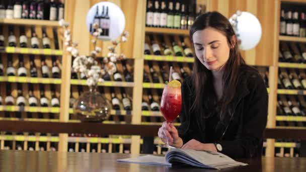 Een jong meisje drinkt een cocktail op een tafel in een restaurant van mode, vrouw rode exotische cocktail drinken — Stockvideo